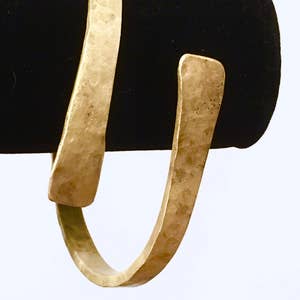 May include: A gold-toned hammered metal cuff bracelet. The bracelet is open and has a slightly curved shape.