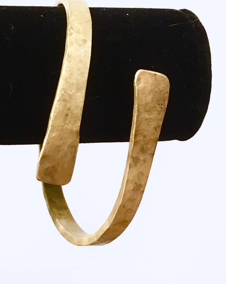 May include: A gold-toned hammered metal cuff bracelet. The bracelet is open and has a slightly curved shape.