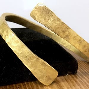 May include: A thick gold-colored metal bracelet with a hammered finish. The bracelet is open and can be adjusted to fit different wrist sizes.