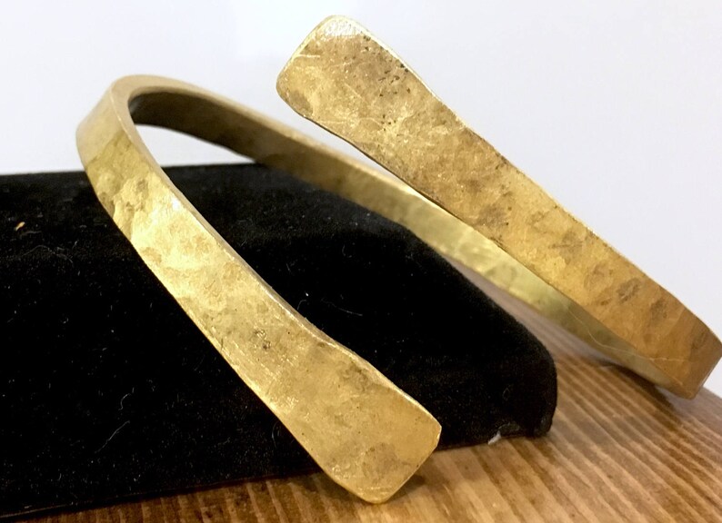 May include: A thick gold-colored metal bracelet with a hammered finish. The bracelet is open and can be adjusted to fit different wrist sizes.