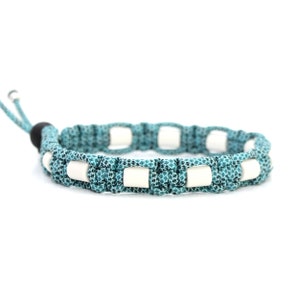 Pode incluir: Um bracelete de paracord azul turquesa com contas brancas. O bracelete tem uma conta preta no fecho.