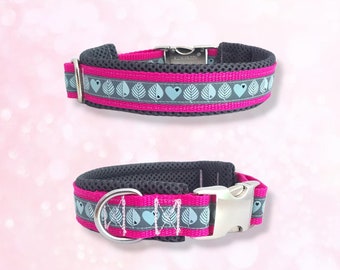 May include: A pink and gray dog collar with a silver buckle and a pattern of blue leaves and hearts. The collar is made of a mesh material.