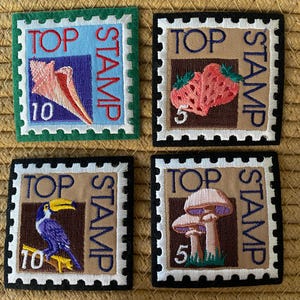 May include: Four embroidered patches in a stamp design. Each patch features a different image: a seashell, strawberries, a toucan, and mushrooms. The patches have the words "TOP" and "STAMP" on them.