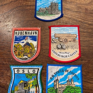 May include: Five embroidered souvenir patches featuring landmarks: Westminster Abbey with blue trim, Copenhagen with red trim, Edinburgh Castle with red trim, Oslo with green trim, and the Tower of London with blue trim, each displaying its name.