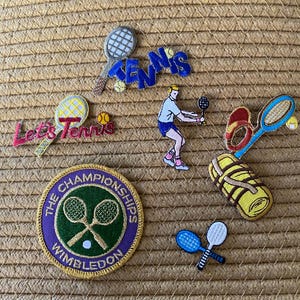 May include: A selection of tennis-themed embroidered patches and designs. Features patches with the word "Tennis", a Wimbledon patch, tennis rackets, tennis balls, and a tennis player figure. The patches are in various colours, including blue, yellow, and green.
