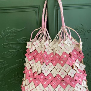May include: A pink and white woven tote bag with a braided handle. The bag is made of a series of small squares with a plus sign in the centre of each square.