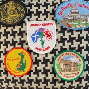 May include: A selection of embroidered patches with Scottish and English themes. Patches include the Scotch Whisky Heritage Centre, St Paul's Cathedral, John O' Groats, a Loch Ness Monster, and Shakespeare's Birthplace in Stratford-upon-Avon.