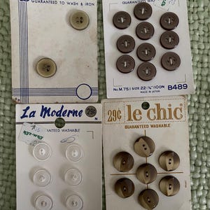 May include: Four vintage retail cards of buttons. One card has two beige buttons labelled Exquisit. One card has ten dark brown buttons labelled La Moderne. One card has six clear buttons labelled La Moderne. One card has seven brown buttons labelled le chic.