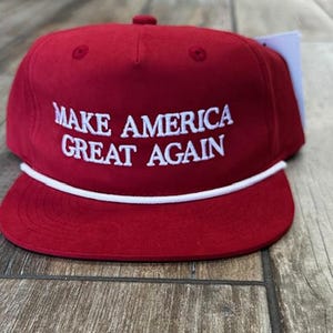 May include: Red baseball cap with a white rope trim and the text "MAKE AMERICA GREAT AGAIN" embroidered in white.