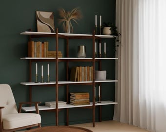 May include: A modern, multi-shelf bookcase with white shelves and dark brown supports. The shelves are filled with books, candles, and decorative items. A round wooden coffee table and a cream-colored armchair are in the foreground.