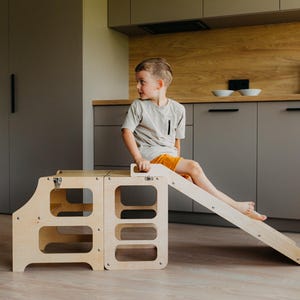 May include: A light-colored wooden climbing structure for children, featuring two modular cube-shaped platforms and a detachable slide. The unit is constructed from smooth, light-toned plywood with rounded edges and metal hardware connectors.
