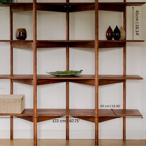 May include: A mid-century modern wooden shelving unit with multiple shelves. The unit is 67.71 inches wide and 67.71 inches tall. The shelves are 11.81 inches deep. The unit is holding decorative items.