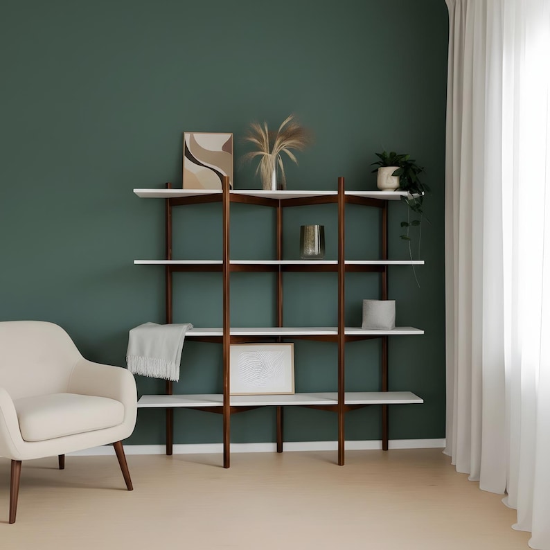May include: A modern, multi-shelf bookcase with a dark wood frame and white shelves. The bookcase is filled with decorative items, including framed art, a vase of dried plants, and a small potted plant. A cream-colored armchair sits to the left.