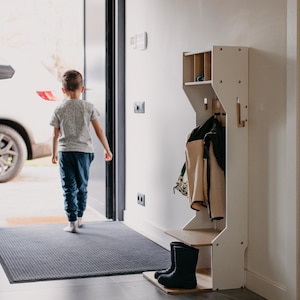 May include: A white wooden coat rack with a shelf, hooks, and a shoe storage area. A child is walking through a doorway in the background.
