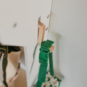 May include: A green strap with a buckle is attached to a white wooden surface. The strap is connected to a small bag with a floral pattern.