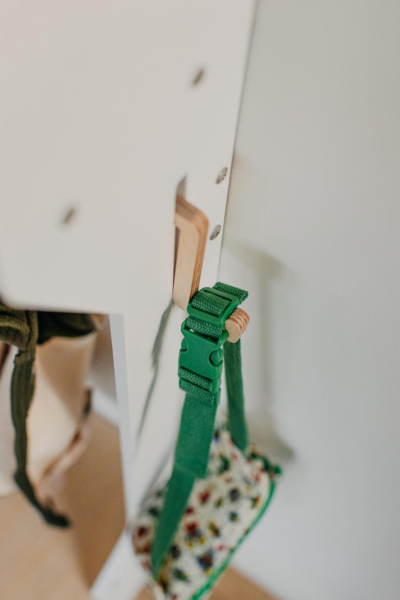 May include: A green strap with a buckle is attached to a white wooden surface. The strap is connected to a small bag with a floral pattern.