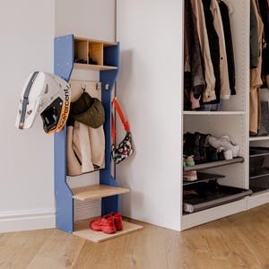 May include: A blue and wood entryway organizer with a helmet, jackets, and a purse hanging on it. Red shoes sit on the bottom shelf. A white closet with clothes and shoes is to the right.