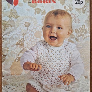 May include: A vintage baby collection pattern cover showing a smiling baby in a white crocheted outfit. The cover features the text "Baby Collection by ROBIN" and a bird illustration.