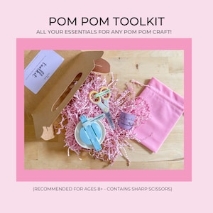 May include: A pink pom pom maker kit with a blue pom pom maker, pink scissors, and a pink drawstring bag. The kit is packaged in a brown box with the words "Pom Pom Toolkit" and "All your essentials for any pom pom craft!" printed on it. The kit is recommended for ages 8 and up and contains sharp scissors.