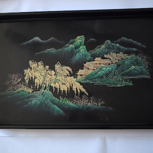 May include: A rectangular black serving tray featuring a detailed landscape illustration. The scene depicts green mountains, a golden willow tree, and a multi-tiered building structure. The artwork is rendered in shades of green, gold, and black.
