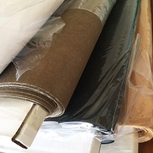 May include: Rolls of different colored paper wrapped in plastic. The paper is brown, white, black, and tan.