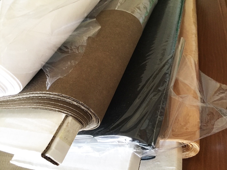May include: Rolls of different colored paper wrapped in plastic. The paper is brown, white, black, and tan.