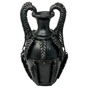 May include: A black ceramic amphora-style vase featuring two upright handles and a decorative exterior cage made of braided black material that wraps around the body of the vessel, creating a textured and layered appearance.