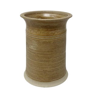 May include: A cylindrical ceramic vase with a flared rim, featuring a textured body covered in fine horizontal ridges. The piece is finished in a mottled tan and brown glaze, transitioning to a smooth, light-coloured base at the bottom.