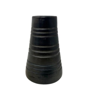 May include: A black ceramic vase with a cylindrical shape and horizontal ridged detailing. The vase has a wide base that tapers upwards to a narrower opening. The dark color and textured surface give it a rustic appearance.