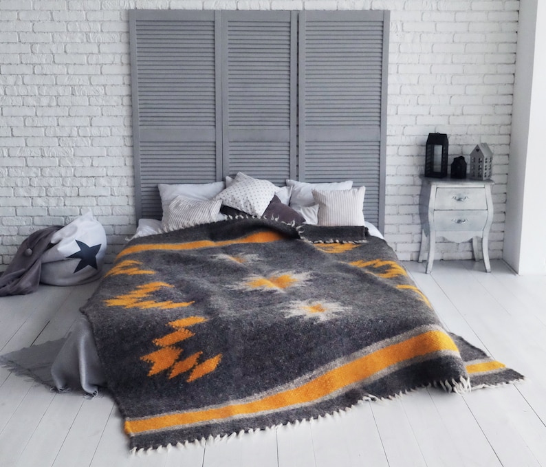 May include: A gray and yellow patterned throw blanket with a fringe border, draped over a bed with white pillows and a gray headboard.