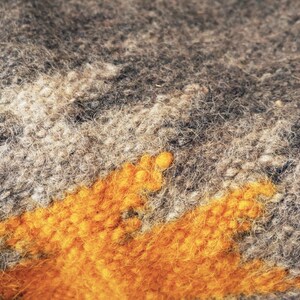 May include: Close-up of a gray and orange knitted fabric with a fuzzy texture. The fabric has a geometric pattern with a large orange section in the center.