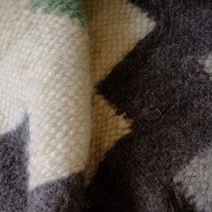 May include: Close-up of a white and gray woven rug with a geometric pattern. The rug is made of soft, fluffy fibers and has a textured surface.