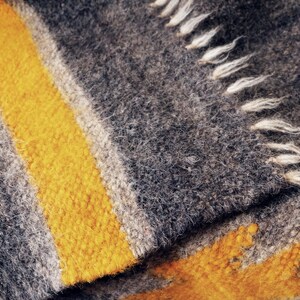May include: Close-up of a gray and yellow woven blanket with a fringe edge. The blanket has a striped pattern with a thick yellow stripe.
