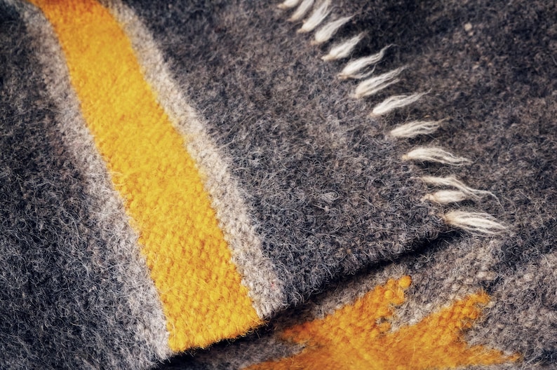 May include: Close-up of a gray and yellow woven blanket with a fringe edge. The blanket has a striped pattern with a thick yellow stripe.