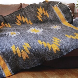 May include: A gray and yellow woven throw blanket with a geometric pattern. The blanket is folded and draped over a brown couch.