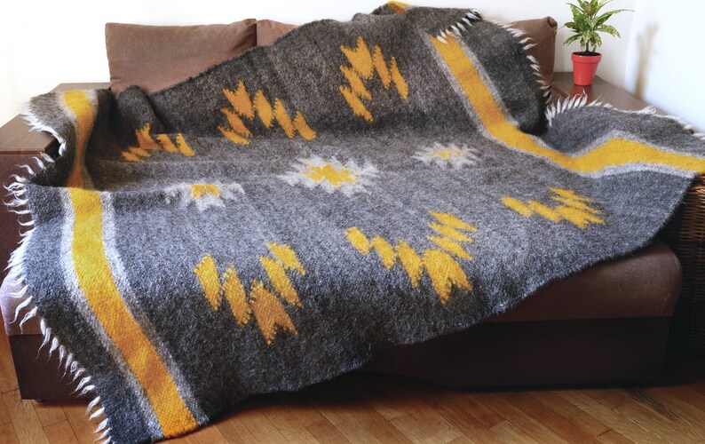 May include: A gray and yellow woven throw blanket with a geometric pattern. The blanket is folded and draped over a brown couch.