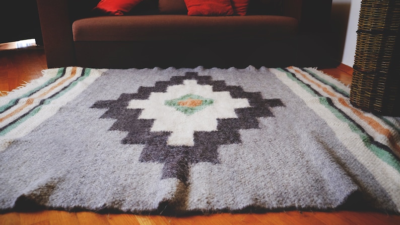 May include: A gray and white patterned rug with a geometric design. The rug has a border of stripes in shades of green, white, and orange.