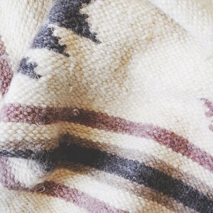 May include: A white, gray, and pink striped woven throw blanket with a geometric pattern.