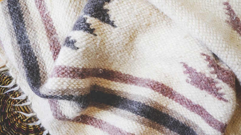 May include: A white, gray, and pink striped woven throw blanket with a geometric pattern.