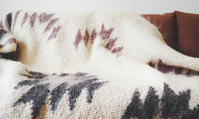 May include: A white throw blanket with a geometric pattern in shades of brown and pink. The blanket is woven with a textured, fuzzy surface.