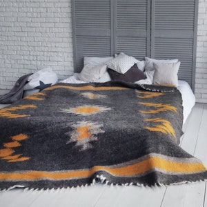May include: A gray and yellow patterned throw blanket with a fringe edge, draped over a white bed with pillows.