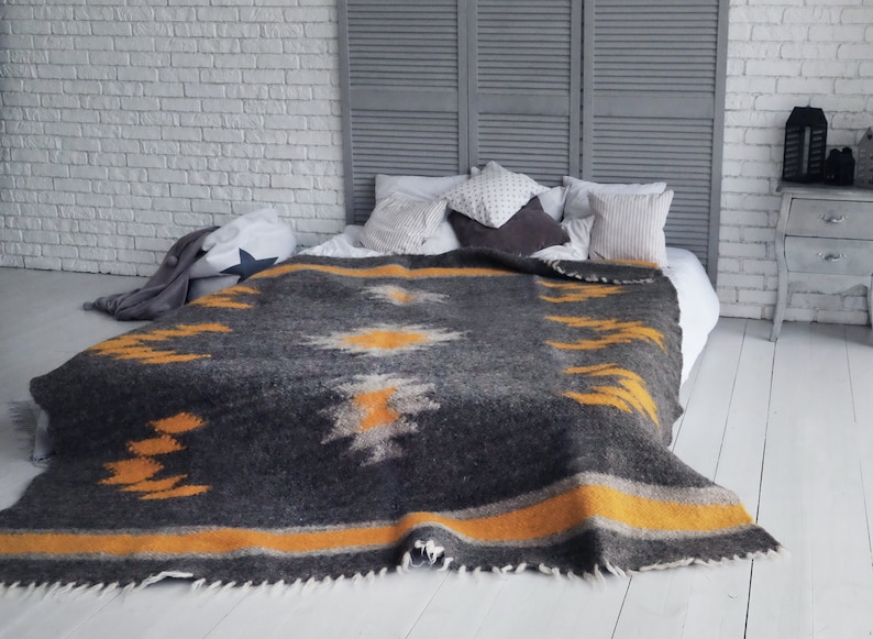 May include: A gray and yellow patterned throw blanket with a fringe edge, draped over a white bed with pillows.