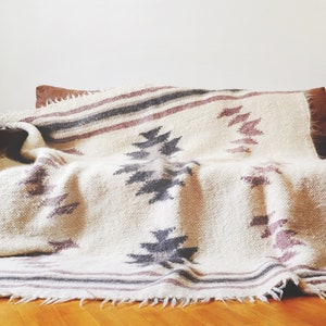 May include: A white throw blanket with a geometric pattern in shades of gray and pink. The blanket is draped over a brown couch.