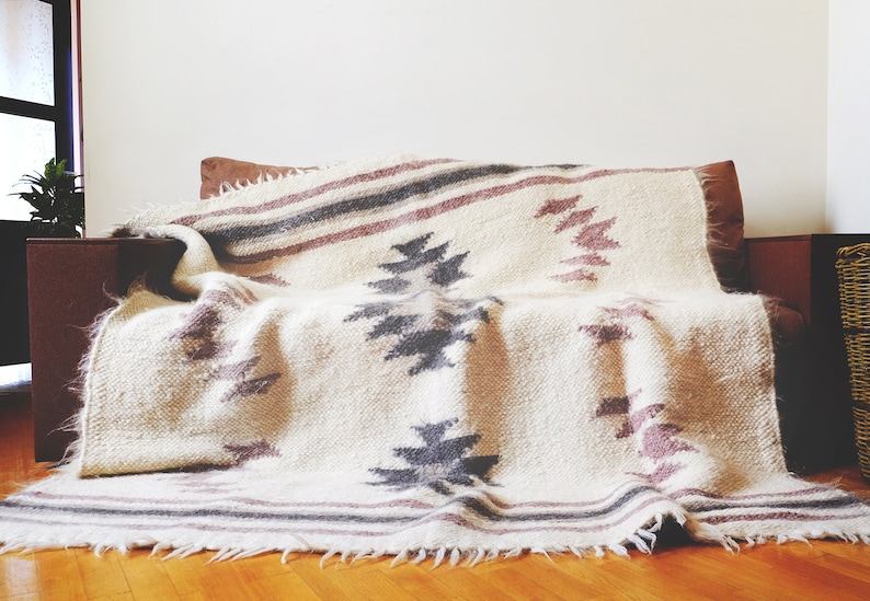 May include: A white throw blanket with a geometric pattern in shades of gray and pink. The blanket is draped over a brown couch.