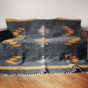 May include: A gray and yellow woven throw blanket with a geometric pattern. The blanket is draped over a couch and has a fringe border.