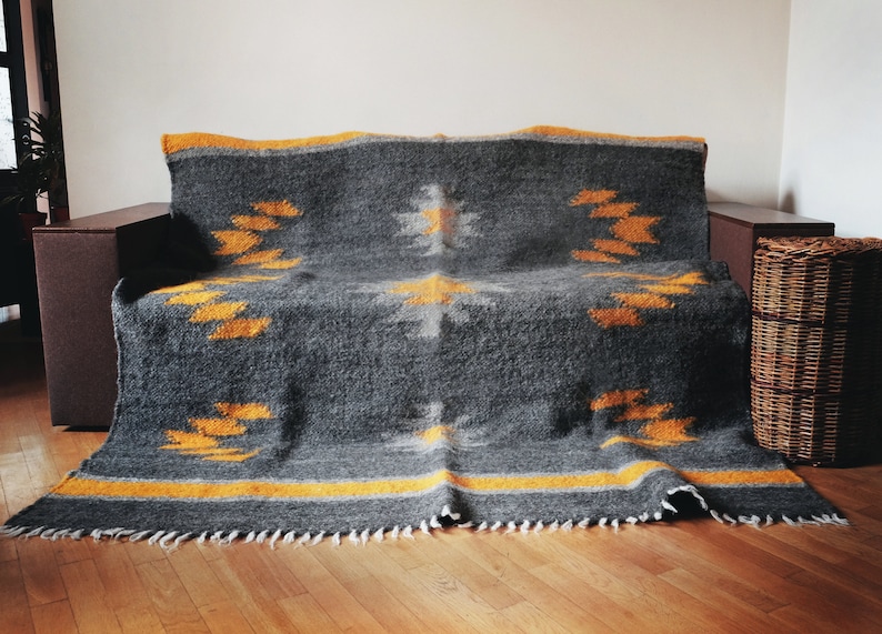 May include: A gray and yellow woven throw blanket with a geometric pattern. The blanket is draped over a couch and has a fringe border.