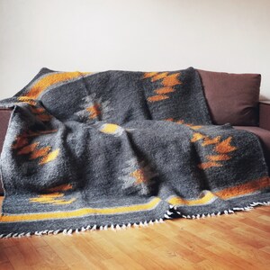 May include: A gray and yellow patterned throw blanket draped over a brown couch. The blanket has a fringe border and a geometric design.