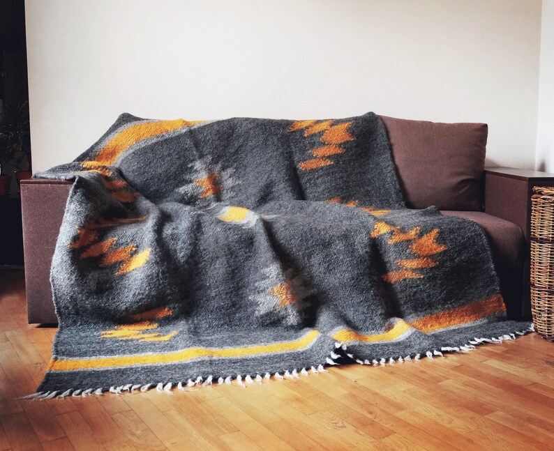 May include: A gray and yellow patterned throw blanket draped over a brown couch. The blanket has a fringe border and a geometric design.