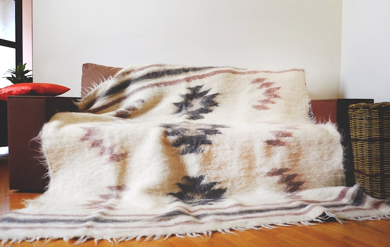 May include: A white, brown, and gray patterned throw blanket with a fringe edge is draped over a brown couch.