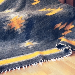 May include: A gray and yellow woven throw blanket with a fringed edge. The blanket is folded and draped over a wooden surface.